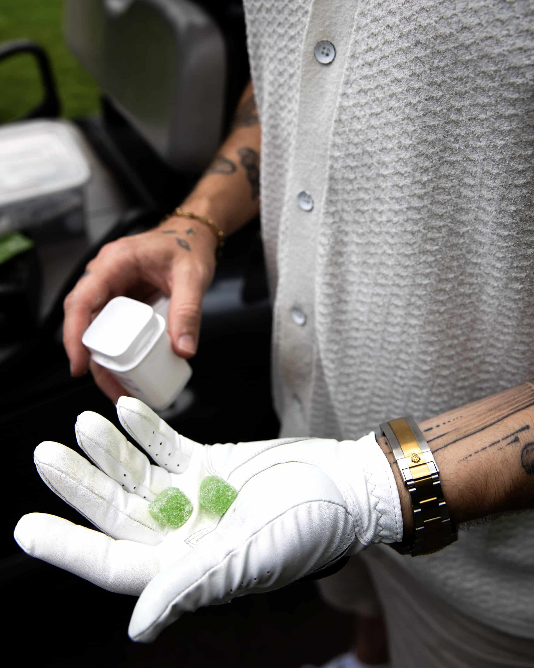 From Consider It Flowers summer 2024 lookbook, a golfer with tattoos is holding Mint Mojito Artisan Gummies in his hand.